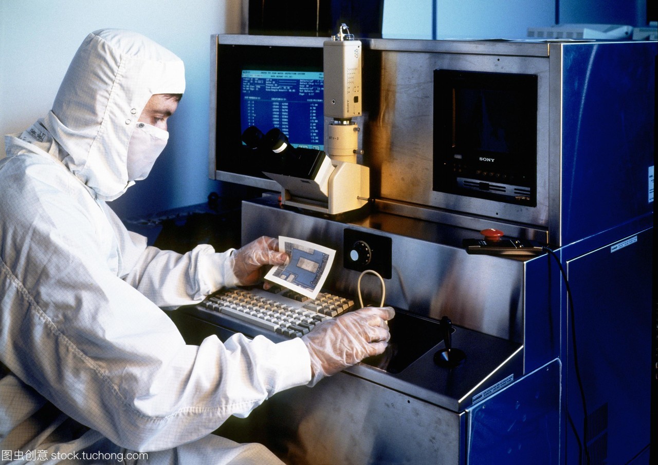 模型發布。硅晶片檢查。一名技術人員拿著一張硅片的部分照片,同時對其微電路進行檢查。他坐在顯微鏡下觀察晶圓的放大。這是一個&ldquo;干凈的房間&rdquo;,技術人員穿著一套身衣,兜帽和面罩。在所有過程涉及人工微電路的制作和測試技術人員穿防護服和手套空氣潔凈室的過濾。即使是最小的塵埃微粒也可能破壞其中的一個微電路。